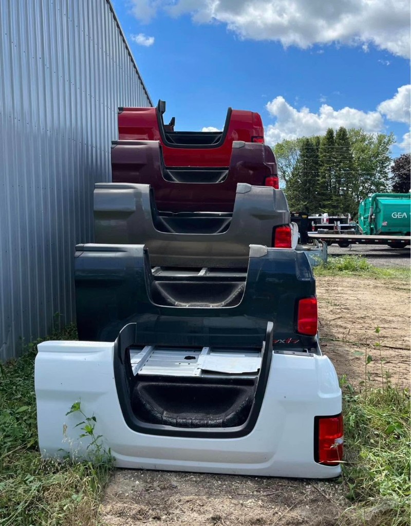 Narrow aisle between red, white, blue and gray pickup beds