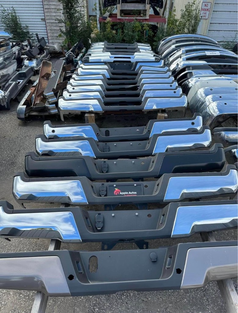 Rows of chrome and black pickup truck bumpers organized outdoors