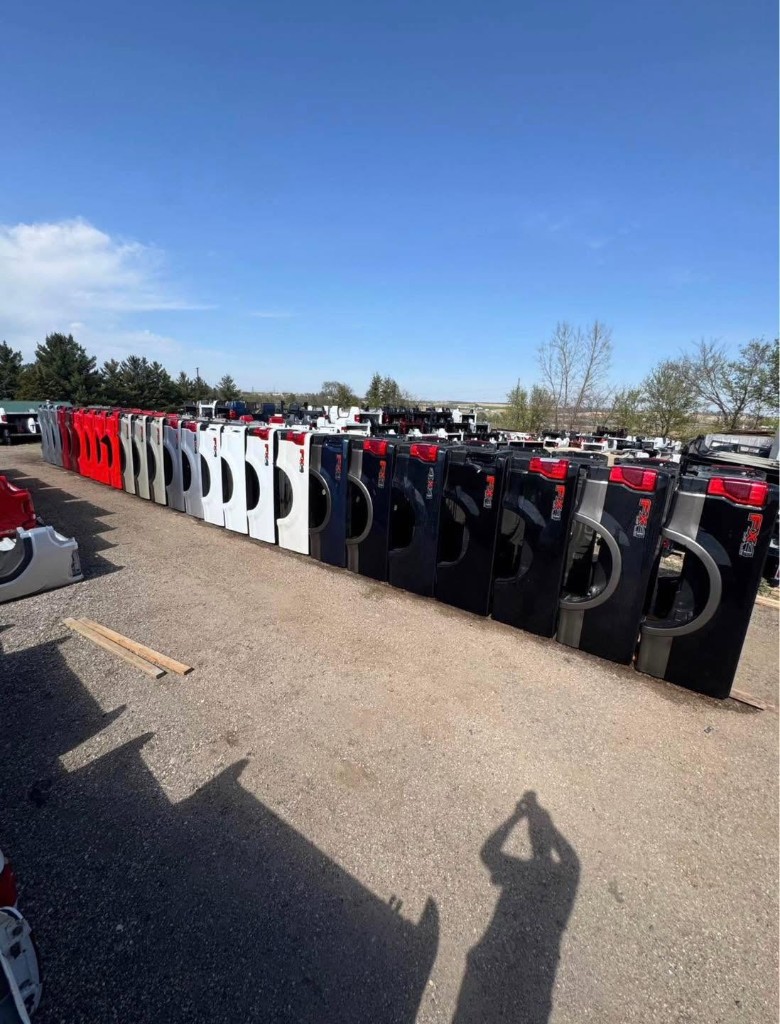 Large outdoor row of pickup truck tailgates in multiple colors