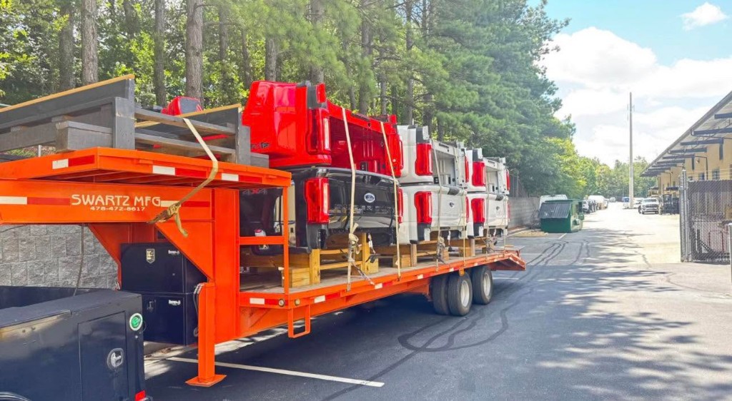 Multiple pickup truck beds secured on a red transport trailer