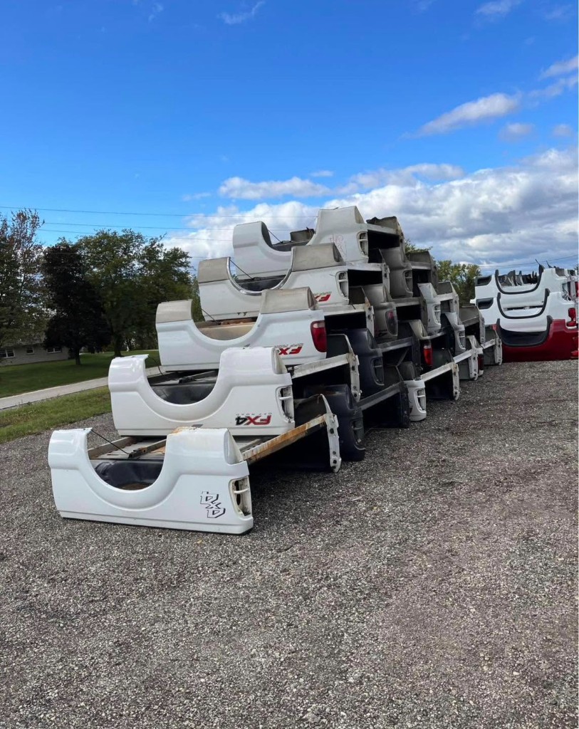Mixed pickup truck beds stacked outdoors beneath a blue sky
